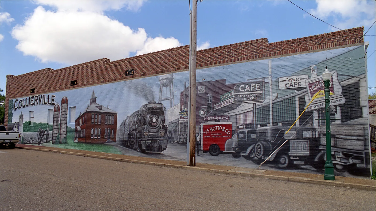 A painted mural of old Collierville, with a steam locomotive, storefronts and vintage cars, on a brick building wall in Collierville.