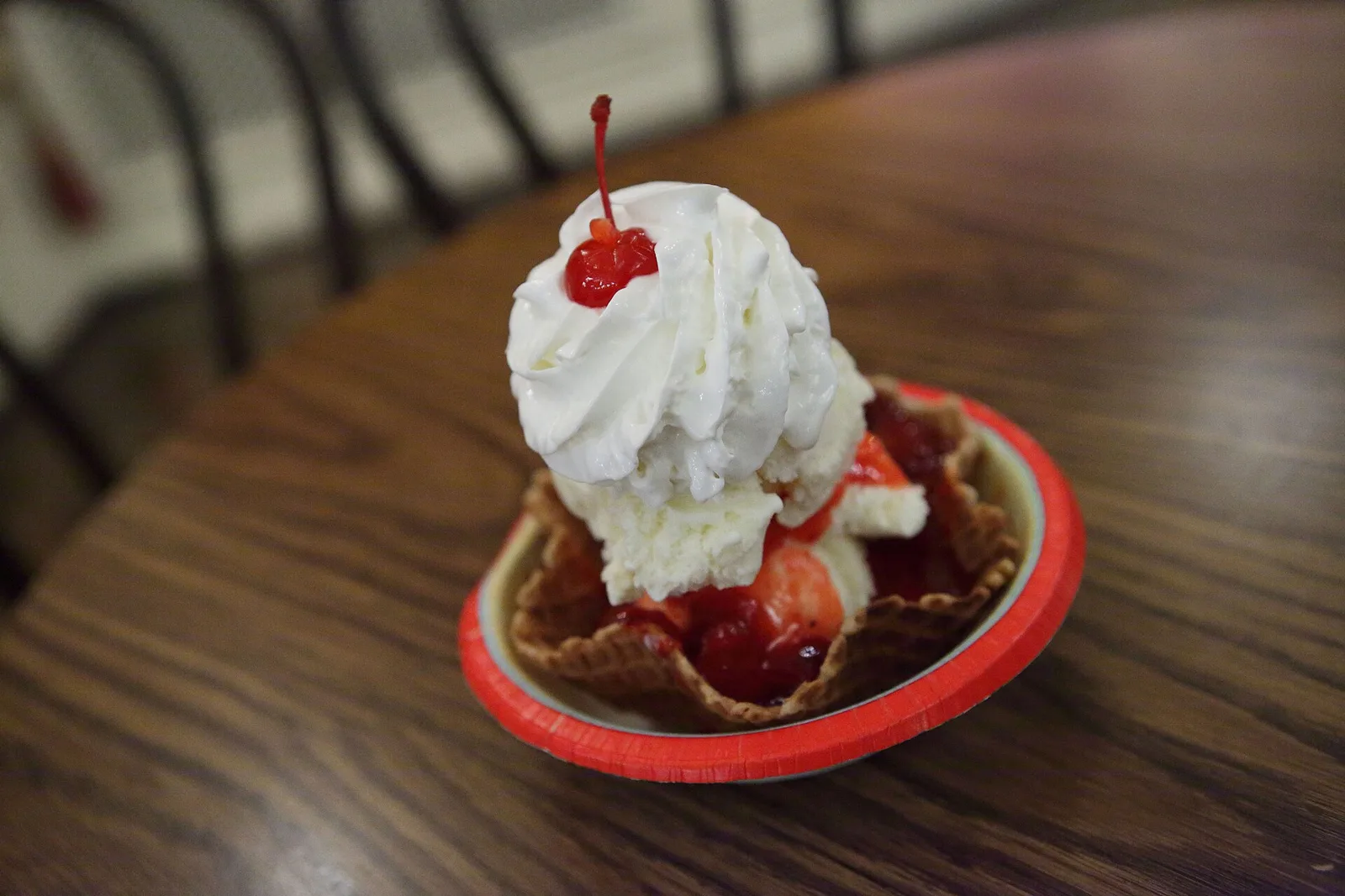 A strawberry ice cream sundae topped with whipped cream, served in a glass dish.