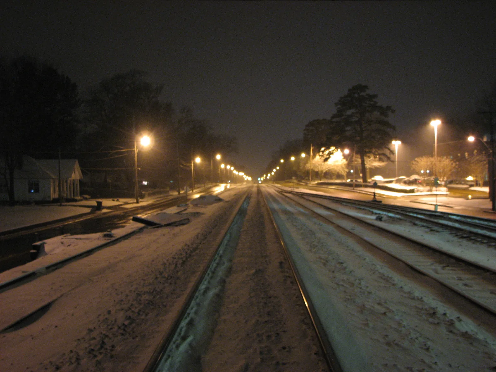 Streetlights glow over snow on the railroad tracks beside the Collierville Town Square at night.