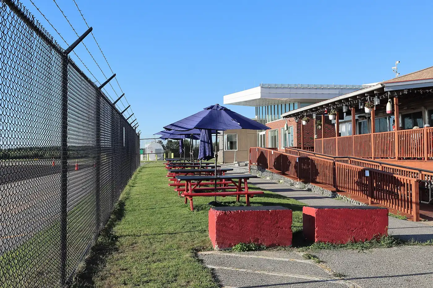 Picnic tables under blue umbrellas beside a restaurant deck at an airport in Southbridge, Massachusetts.