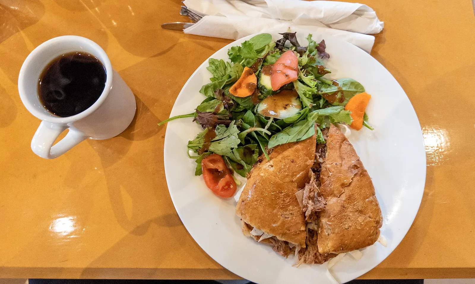 A pulled pork sandwich with a side salad and a cup of coffee at a cafe in Toronto.