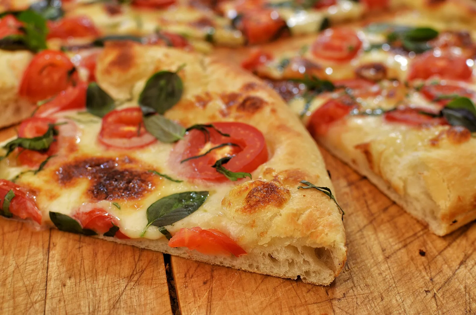 A sliced Margherita pizza topped with tomato, mozzarella and basil on a wooden board.